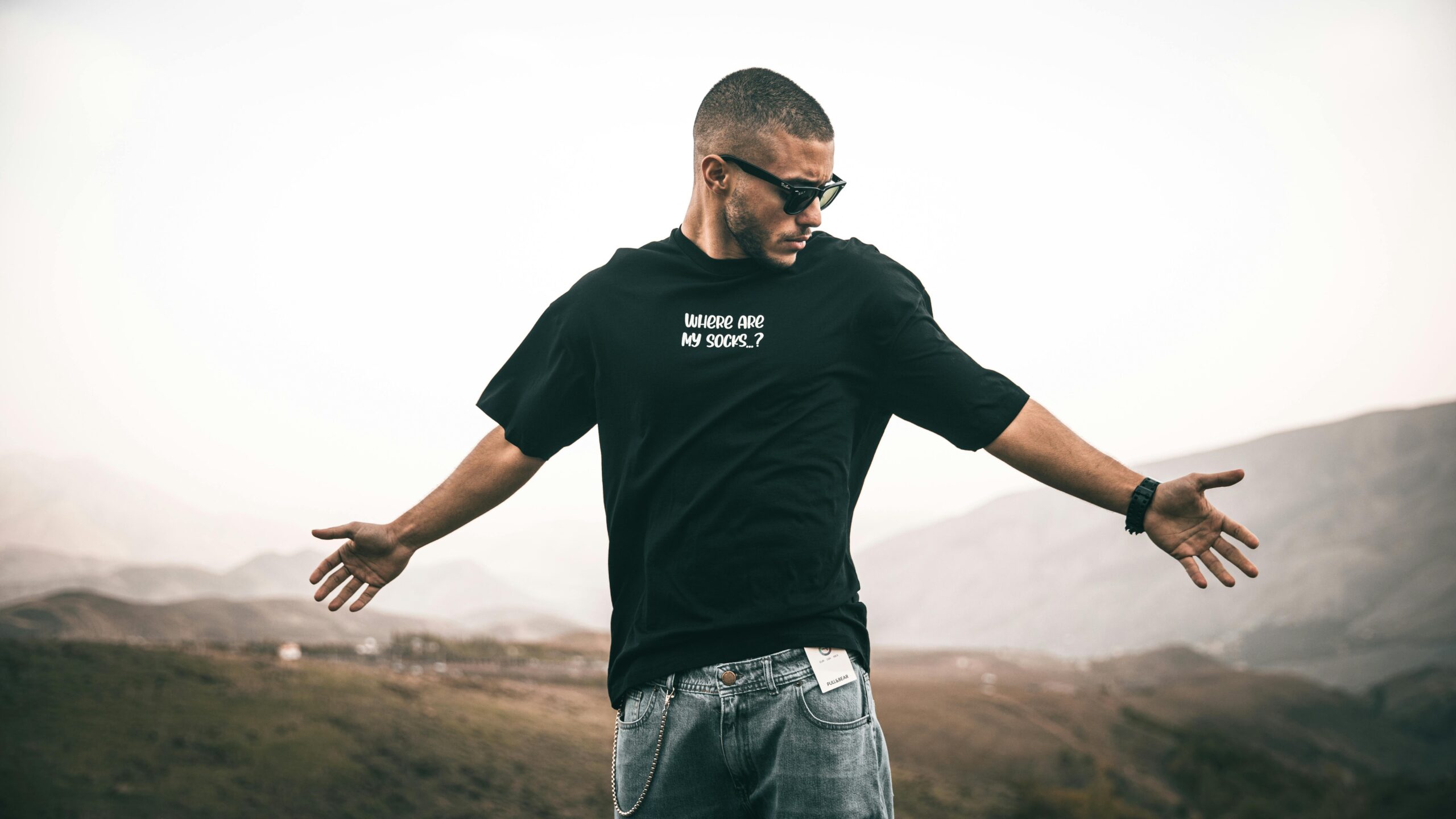 Home Fashionable young man posing confidently outdoors in Iran wearing sunglasses and graphic t-shirt.