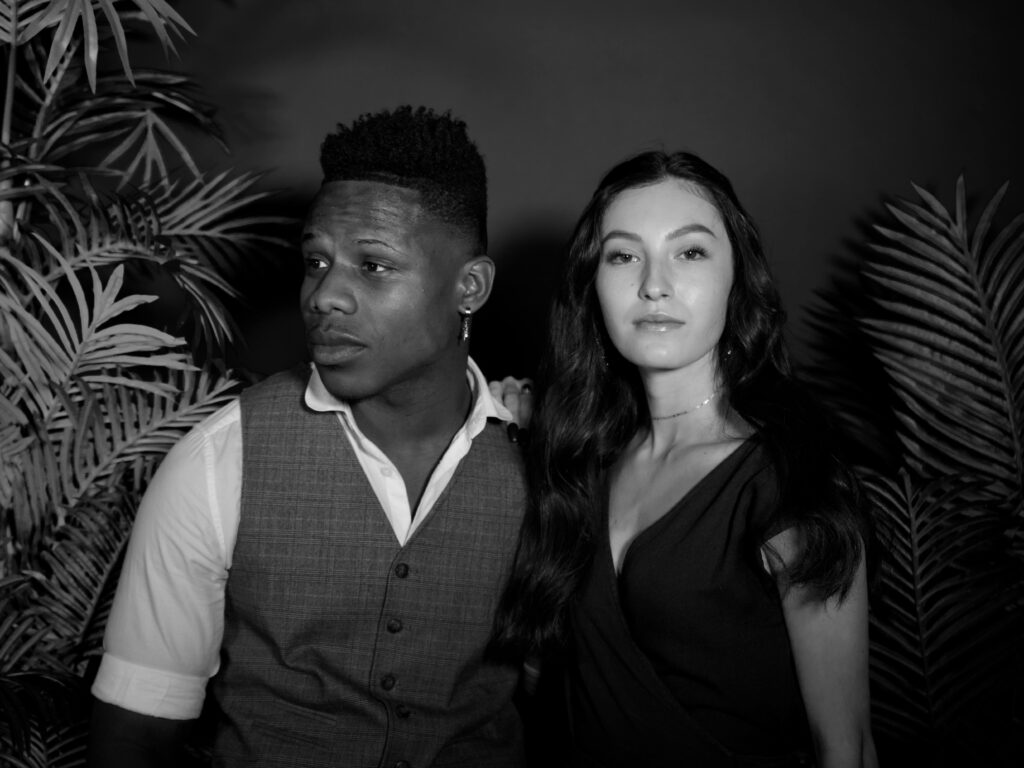 Stylish black and white portrait of a couple standing together, surrounded by foliage.