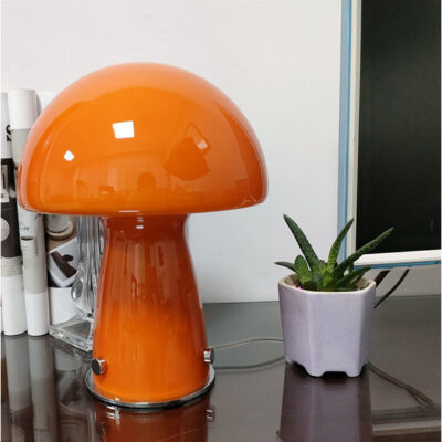 Orange Molanizzi mushroom lamp on a glass table with a potted plant