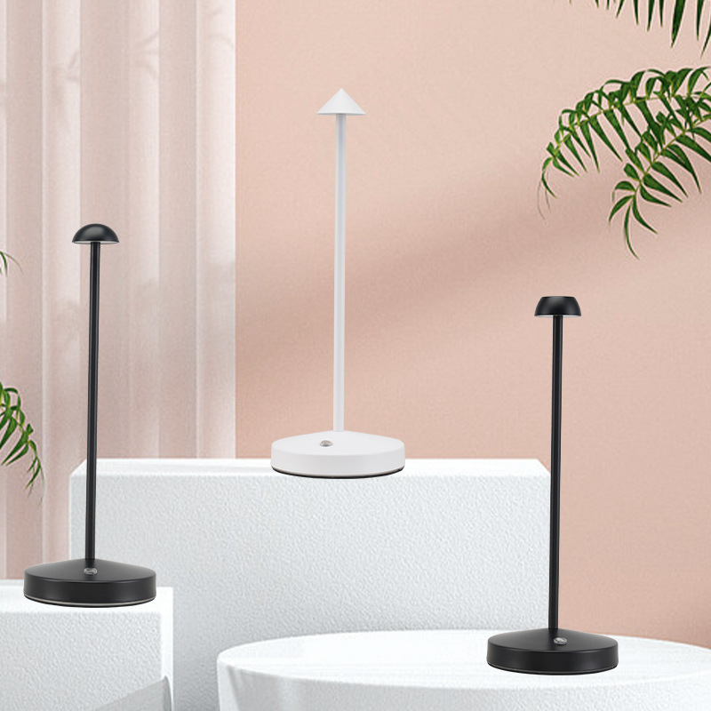 Three modern black and white table lamps on white surfaces against a pink background