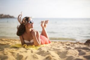 Woman in sunglasses sunbathing on a beach, enjoying the summer breeze and sunlight.